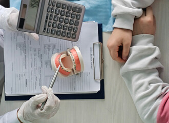 A dentist discusses treatment options for teeth with braces with a patient using a dental model and calculator concept