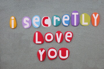I secretly love you, creative message composed with multi colored hand painted stone letters over green sand