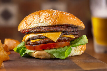 Triple cheeseburger seen up close with fastfood background with fried food and beer blurred horizontally with warm, bright colors