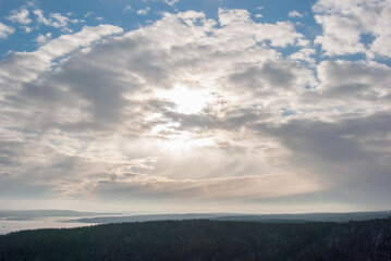 Fototapeta premium Dramatic view of the sky, bright rays of the sun shine through the clouds illuminating the forest distance.
