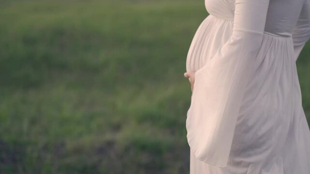 Side shot of pregnant woman walking in a green field