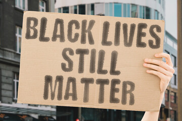 The phrase 'Black Lives Still Matter' on a banner held by a person. Racial equality and justice. Equality. Liberation. Community. Justice. Resilience. Solidarity. Dignity