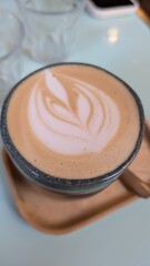 A beautifully crafted latte in a ceramic cup, featuring intricate latte art on the creamy surface, placed on a wooden tray, evoking a cozy coffeehouse ambiance