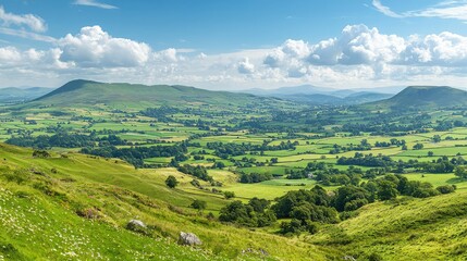 Fototapeta premium Stunning panoramic view of lush green hills and valleys under a bright blue sky, featuring rolling landscapes and scattered clouds in a serene countryside setting.