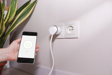 Woman turning on smart plug using her smartphone. Smart home concept. 