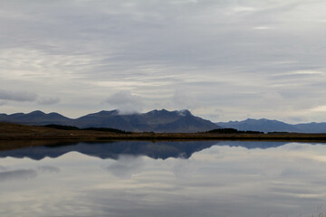 A tranquil Icelandic lake reflects the surrounding mountains in its still waters