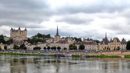 Saumur: Historic European Chateau Overlooking Serene Riverside Town Under Cloudy Sky