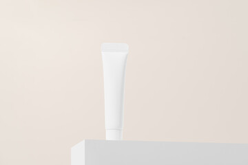 White cream tube mockup on white pedestal on beige isolated background. The concept of cosmetics for skin care around the eyes and face, moisturizing, nourishing and anti-aging. Image for your design.