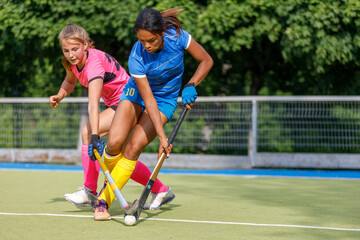 Two young female athletes compete in intense field hockey match during sunny day
