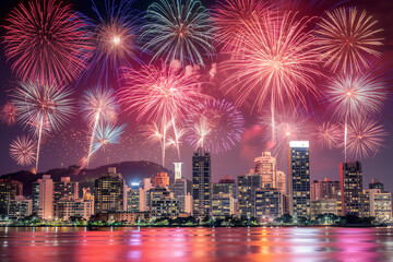 Fireworks display over city skyline at night with reflections on water
