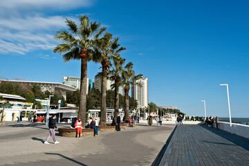 Warm sunny day on the waterfront promenade with palm trees and people enjoying leisure activities - Sochi, Russia April 14, 2024