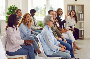 Group of diversity business people sitting in a row on chairs and listening to their colleague or...