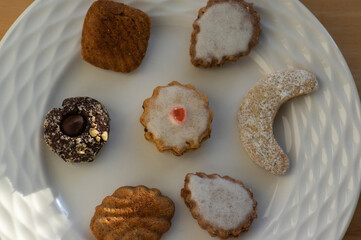 Various kinds of tasty Christmas chocolate, nuts and filled cookies on white plate