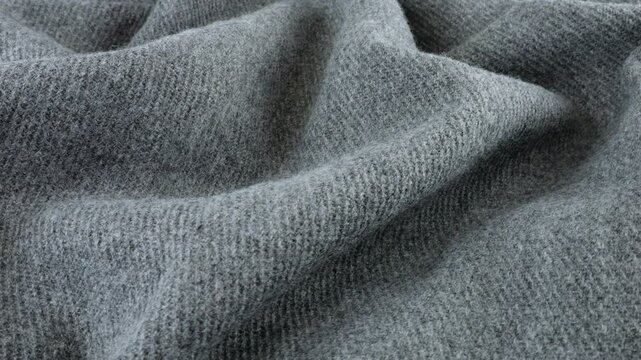 Top view of the soft folds of textured gray wool fabric rotated on the display case. Textile background on cold weather, warm clothes, comfort, accessories and design theme.