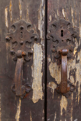 Description: Two intricately designed door handles, crafted from wrought iron, adorn a weathered wooden door