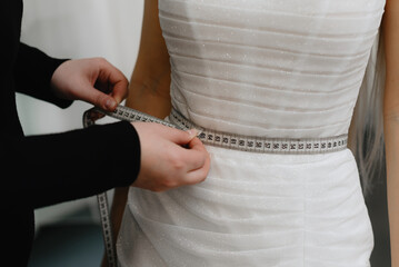 wedding salon administrator measures bride waist at fitting in salon, cropped, no face, preparing...