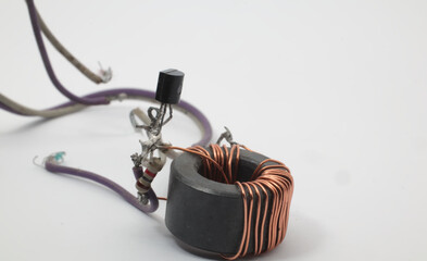 A ferrite core toroid ring with copper windings connected to a resistor and a transistor on a white...