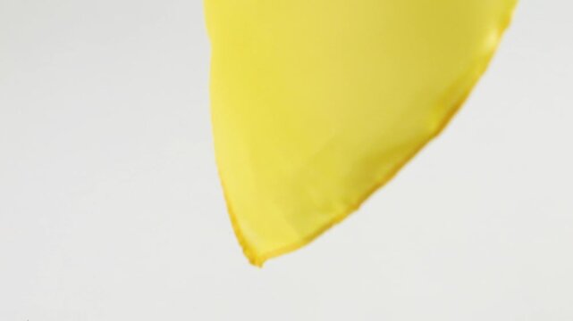 A light bright yellow scarf made of natural silk slowly falls in soft folds onto a white background. Slow motion.