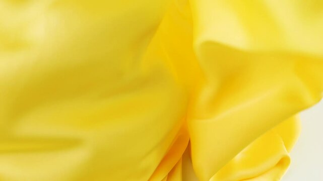 A light bright yellow scarf made of natural silk slowly falls in soft folds onto a white background. Slow motion.