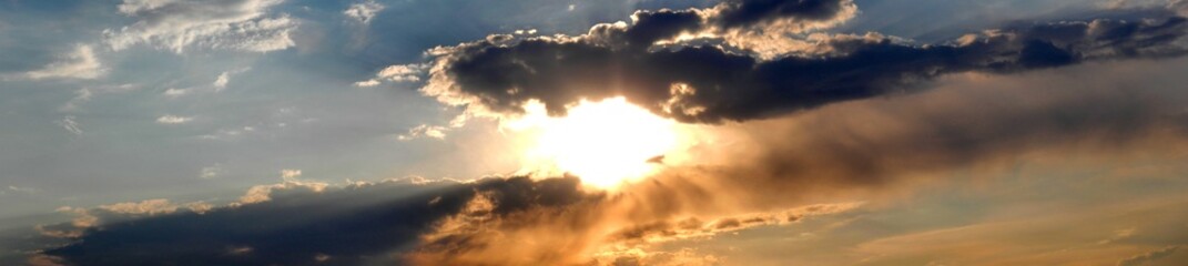 Blue and orange sky with sun and clouds during sunset - natural air space panorama. Topics: weather, meteorology, solar energy, sunlight, evening