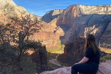 A woman admiring the beautiful views of Zion National Park in Utah, United States, with views of the valley and surrounding red rock face.  One of the most beautiful landscapes in the United States.