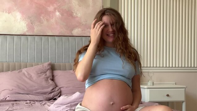 beautiful pregnant woman wakes up and pulls up in the morning in bed in the bedroom and strokes her belly, 3 trimester