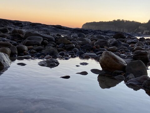 Pett Level Beach at Sunset. With pool of sea ocean water and rocks in foreground. Winchelsea Beach meets the cliffs a petrified forest visible at low tide, on the South coast of England East Sussex UK