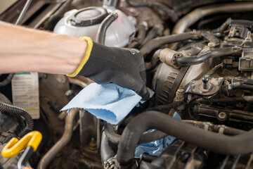 Mechanic in gloves servicing a car engine with tools and cloth in a well-lit garage, concept of...