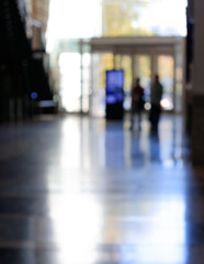 Out of focus people walking in a corridor at the entrance of a bright building. Long reflections on the floor.