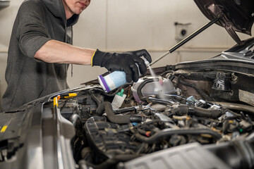 Mechanic wearing gloves sprays cleaner on a car engine  in a garage. Concept of vehicle maintenance
