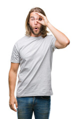 Young handsome man with long hair over isolated background doing ok gesture shocked with surprised face, eye looking through fingers. Unbelieving expression.