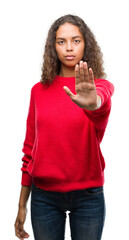 Young hispanic woman wearing red sweater doing stop sing with palm of the hand. Warning expression...
