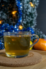 A transparent cup of green tea surrounded by citrus fruits and a Christmas tree, creating a festive atmosphere.
