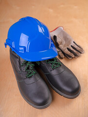 Helmet, gloves and safety shoes for construction workers on a wooden table.