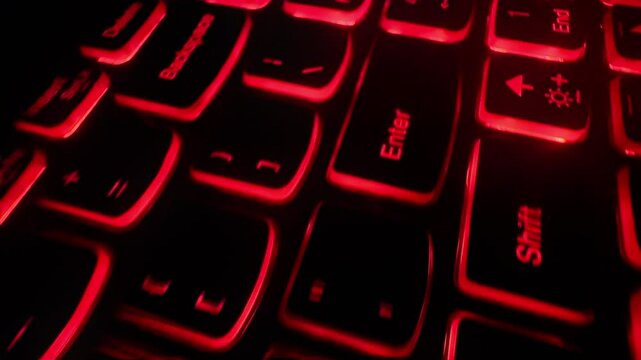 Extreme closeup of an old red backlit laptop computer keyboard. Dolly shot. 80s 90s stylized video with scanlines. Hacking,, thriller, computer technology theme. Cinematic filmic look. 