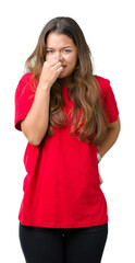 Young beautiful brunette woman wearing red t-shirt over isolated background smelling something...