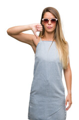 Beautiful young woman wearing sunglasses and denim dress with angry face, negative sign showing dislike with thumbs down, rejection concept