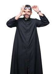 Young Christian priest wearing sunglasses over isolated background doing ok gesture with hand smiling, eye looking through fingers with happy face.