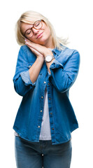 Young beautiful blonde woman wearing glasses over isolated background sleeping tired dreaming and posing with hands together while smiling with closed eyes.