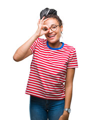 Young braided hair african american girl wearing glasses over isolated background doing ok gesture with hand smiling, eye looking through fingers with happy face.