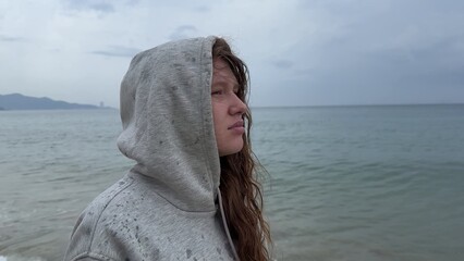 Young woman shivering and trembling from cold rainy weather at summer vacation on beach, sea