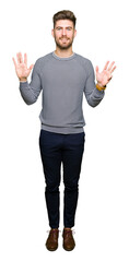 Young handsome man wearing stripes sweater showing and pointing up with fingers number nine while...