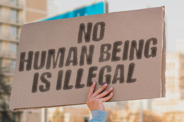 The phrase 'No human being is illegal' displayed on a banner held by a person, advocating for...