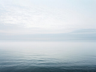Fototapeta premium A serene panoramic view of a calm ocean under a foggy morning sky, blending soft hues with a tranquil, infinite horizon. Generative AI