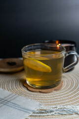 A cup of tea with a lemon slice, accompanied by a burning candle in the background, creating a cozy and relaxing atmosphere.
