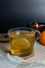 A cup of tea with lemon, accompanied by a burning candle and a tangerine in the background, creating a warm, cozy atmosphere.