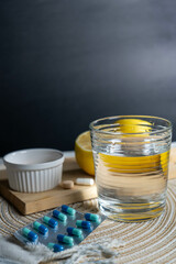 A glass of water with vitamins, two lemons, and a blister pack of tablets on a table, evoking themes of health and hydration.