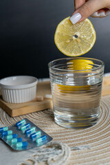 A lemon slice being dropped into a glass of water, surrounded by vitamins and tablets, symbolizing health, wellness, and immune support.