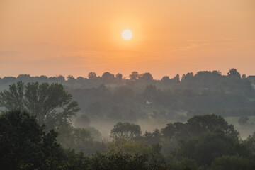 Orange sunrise over treetops and misty hills