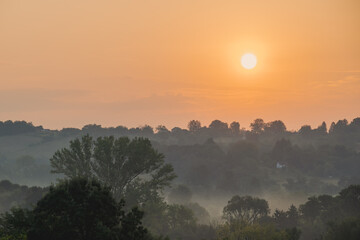 Orange sunrise over treetops and misty hills